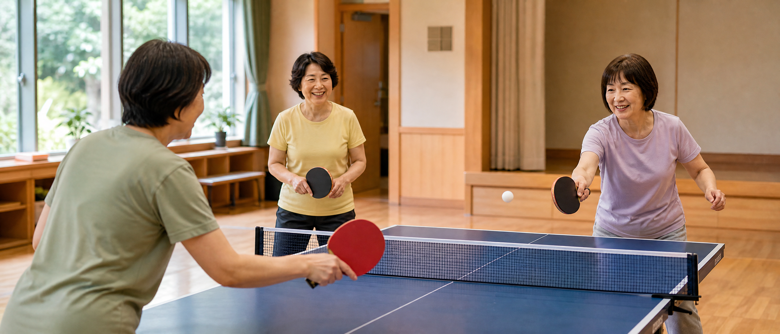 50代から60代の女性が地域の体育館で卓球を楽しむ様子